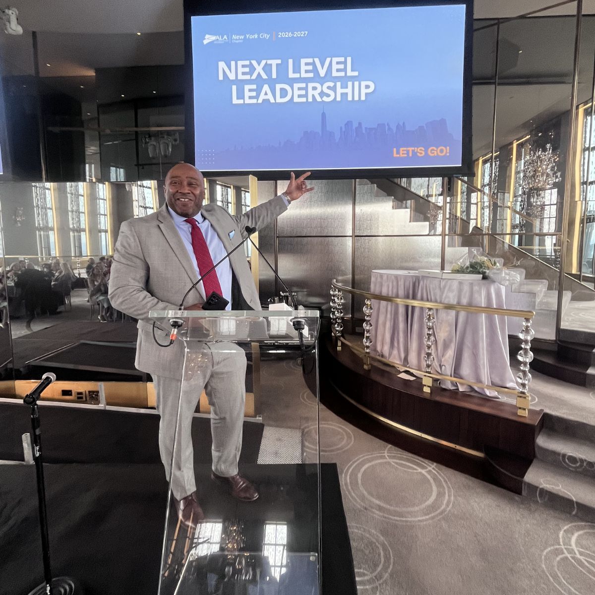 Tirek J. Gayle at the podium addressing ALA New York City, with the 2026–2027 Next Level Leadership presentation behind him